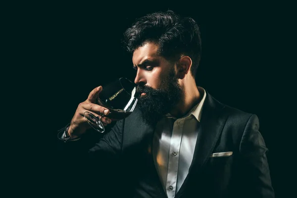Fröhlicher bärtiger Mann trinkt teuren Cognac. Altes traditionelles Whiskeygetränk - Gentlemen Drink. Eleganter und stilvoller Mann in klassischer Kleidung mit Glas und Cognac in der Hand. — Stockfoto