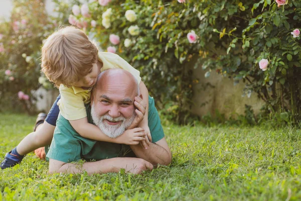 Avô feliz dando ao neto passeio de piggyback em seus ombros e olhando para cima. Criança feliz com o avô brincando ao ar livre . — Fotografia de Stock