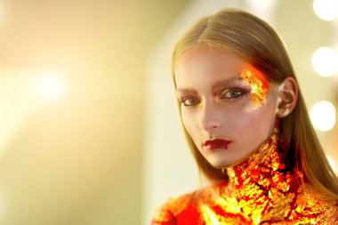 Kanlı dudaklı ve altın gözlü vampir kadın. Cadılar Bayramı 'nda altın renkli makyajlı manken kız. Parlak metalik parlak altın makyaj..