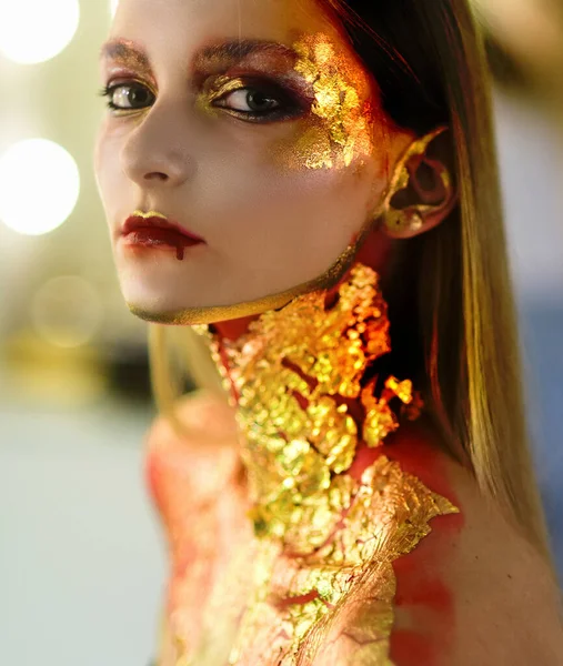 Arte Cara de niña de piel dorada - retrato de Halloween de cerca. Bruja de Halloween. Mujer de Halloween de oro. Chica modelo de moda de Halloween con maquillaje dorado . — Foto de Stock