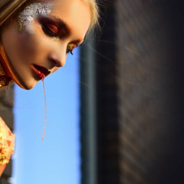 Güzel altın gözler kırmızı kanlı dudaklar. Cadılar Bayramı parti sanat tasarımı. Parlak makyajlı cadılar bayramı cadısı. Cadılar Bayramı makyajı. Havalı Cadılar Bayramı Parlayan altın cilt makyajı.