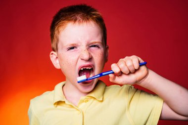 Gülen çocuk kırmızı zemin üzerine izole diş fırçası ile bir diş olmadan. Diş kavramı - genç kız dişlerini fırçalama boş beyaz gömlek gülümseyen. Küçük çocuk Dişlerini fırçalıyor.