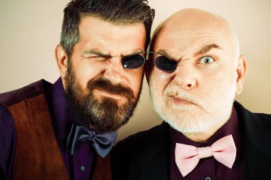 Nesiller. Eski baba ve oğul. Kameraya bakarak komik büyük baba ve Yetişkin oğlu. Nesiller kavramı. Gülümseyen kıdemli bayım ve retro gözlüklü genç erkekler. Farklı yaş nesillerin aile.