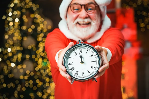 Porträt des überraschten und lustigen Weihnachtsmannes. Lächelnder Weihnachtsmann zeigt Wecker mit fünf Minuten vor zwölf. Fünf Minuten vor Neujahr oder Weihnachten Mitternacht. — Stockfoto