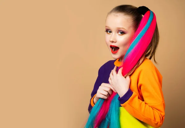 Maquiagem menina colorida e cabelo arco-íris. Foto de moda de modelo europeu lindo pouco com design de arte. Estúdio tiro de menina quente olhando para a câmera, isolado no fundo de cor . — Fotografia de Stock