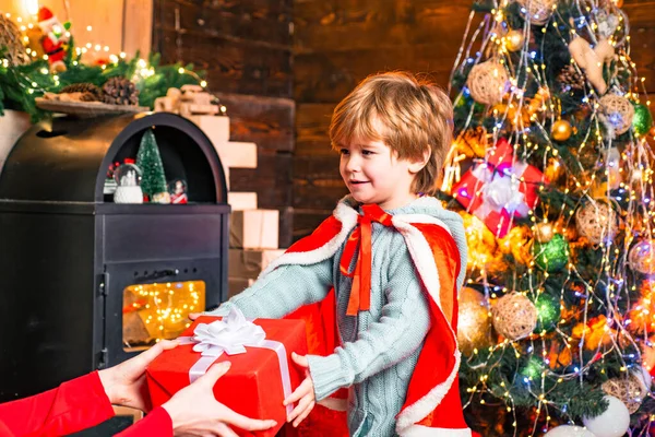 Mały chłopiec otrzymuje prezent noworoczny na dekorowanym tle wnętrza Bożego Narodzenia. Piękna choinka i kominek. Wigilia. ferie zimowe. — Zdjęcie stockowe