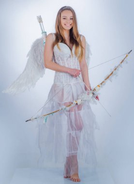 Aşk tanrısı kızı aşk okuyla birini hedef alıyor. Hafif arka planda melek gibi giyinmiş bir kız. Aşk konsepti. Beyaz kanatlı bir melek..