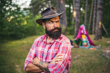 Hispter tarzı. Ormanda çekici bir turist. Saç sakalı bakımı. Moda portresi adamı. Yakışıklı sakallı erkek. Uzun gür siyah sakallı ve bıyıklı yakışıklı, güçlü, stil sahibi bir adam. Doğal arkaplan.
