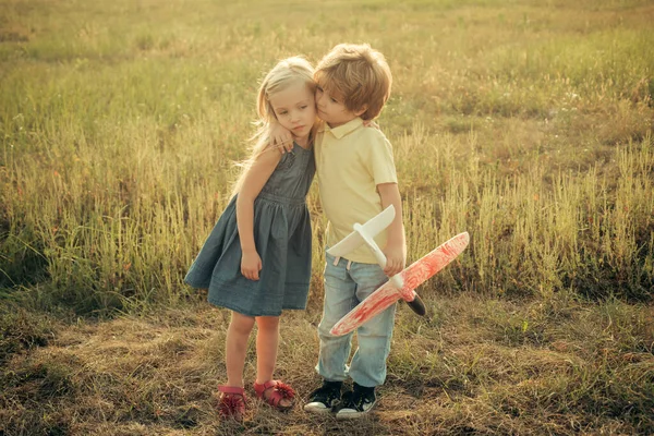 Belo pequeno par - rapaz e menina abraçando. Conceito de imaginação de sonho da infância. Crianças bonitas andando no campo dourado de trigo em um dia ensolarado de verão. História de amor . — Fotografia de Stock