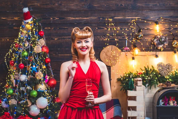 붉은 크리스마스 드레스를 입은 아름다운 금발의 여성이 빛나는 크리스마스 트리 옆에 장식 이 있는 방에 서 있다.. — 스톡 사진