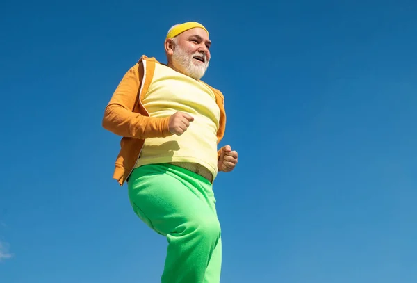 Elderly man practicing sports on blue sky background. Cheerful senior jogging in sportswear on sky background. Age is no excuse to slack on your health.