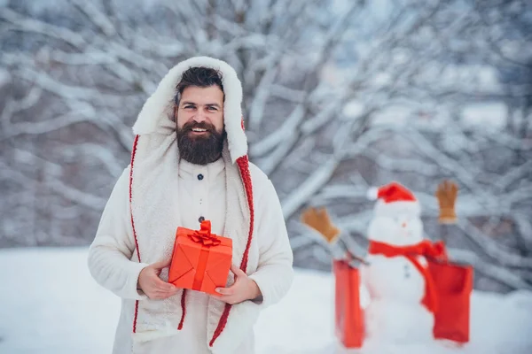 Compras de Navidad con bolsa de compras. Venta de Navidad y descuentos. Hombre de invierno guapo con regalo y muñeco de nieve en el helado parque de invierno . — Foto de Stock