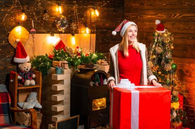 Beautiful charming woman received huge Christmas present gift box with surprise inside it. Portrait of happy positive woman against wooden background in the decorated room.