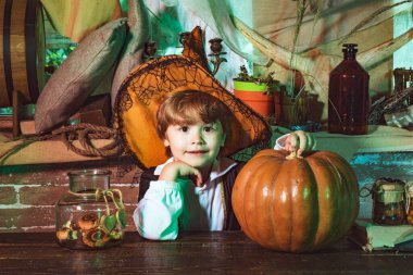 Karnaval kostümlü komik çocuk içeride. Cadılar Bayramı kostümü giymiş bir çocuk ve balkabağı eski ahşap bir ev. Çocuk Cadılar Bayramı balkabağıyla eğleniyor..