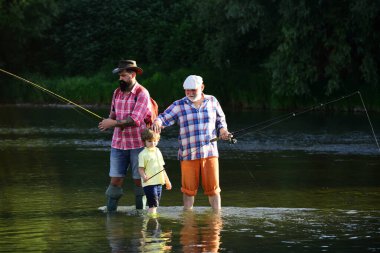 Nehirde balık tutmak. Baba oğluna nehir manzarası ve manzaraya karşı balık tutmayı öğretiyor. Genç-yetişkin kavramı. Baba, oğul ve büyükbaba balık tutuyor..