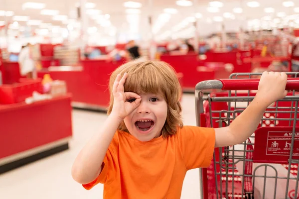 Ragazzo americano sorridente con carrello della spesa con in negozio di alimentari. Bambino carino con carrello della spesa con prodotti . — Foto Stock