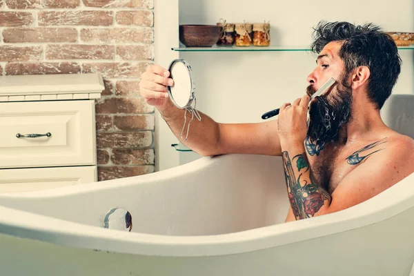 Morgonbehandlingar. Skäggig man med skägg med spegel i handen. Grooming skägg. Hudvård i badrummet. — Stockfoto