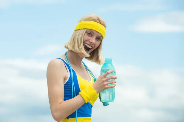 Athlète joyeuse joyeuse joyeuse regardant avec confiance dans la caméra tout en tenant une bouteille d'eau, portant des vêtements jaune-bleu s'entraînant dans la rue . — Photo