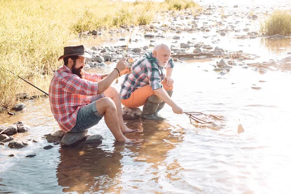 Portret van een vrolijke oudere man die vist. Gelukkige visser met baard in het water. Vissen als vakantie. Vissers hebben lange hengels. Portret van twee mannen op vakantie. Goede winst. — Stockfoto