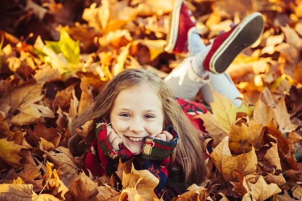 Miúda em folhas de bordo douradas. Brincando com folhas. Menina bonita criança feliz se divertindo no parque de outono entre as folhas caídas. Posando . — Fotografia de Stock