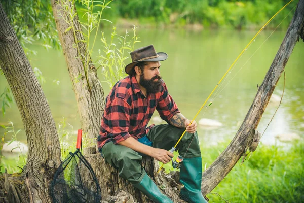 Man fiskar på floden. Sitter ensam under fiskeprocessen på piren nära sjön. Gammal man som flugfiskar. Mot bakgrund av vattnet med en reflektion av skogen. — Stockfoto