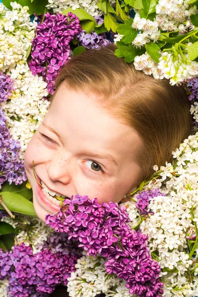 Divertido retrato facial de hermosa niña guiñando un ojo. Chica adolescente con ramo de lila púrpura y blanca. Cara graciosa. Muestra cómica, emoción divertida, cara loca . — Foto de Stock