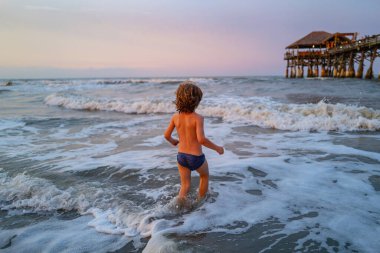 Doğada deniz, kum ve mavi gökyüzü olan bir çocuk. Çocuk dışarıda yüzmeyi öğreniyor. Yaz tatili ve seyahat konsepti.