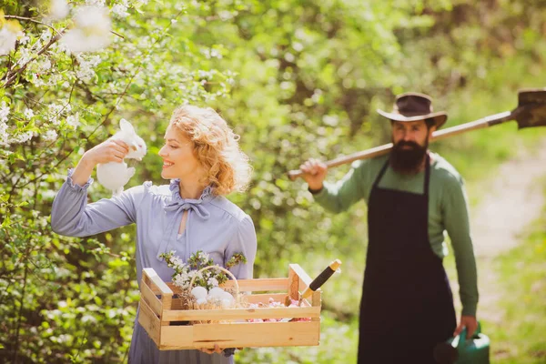 Bild von zwei glücklichen Bauern mit Instrumenten. Frau und Mann verbringen Zeit im Obstgarten. Ein Bauer und seine Frau stehen auf ihrem Feld. — Stockfoto