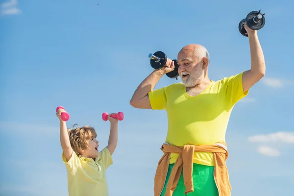 Senior fitness man training with dumbbells isolated on blue background. Happy little boy and grandfather lifting dumbbells on blue sky background.