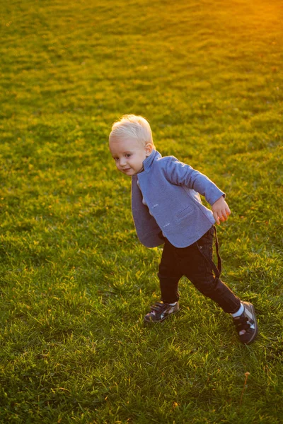 Lindo niño caminando en el prado de hierba verde atardecer puesta del sol. Caminando hasta el atardecer. El chico disfruta paseando por el parque. Juegos activos de jardín de infantes. Concepto de cuidado infantil. Feliz infancia. Niño chico le gusta caminar — Foto de Stock