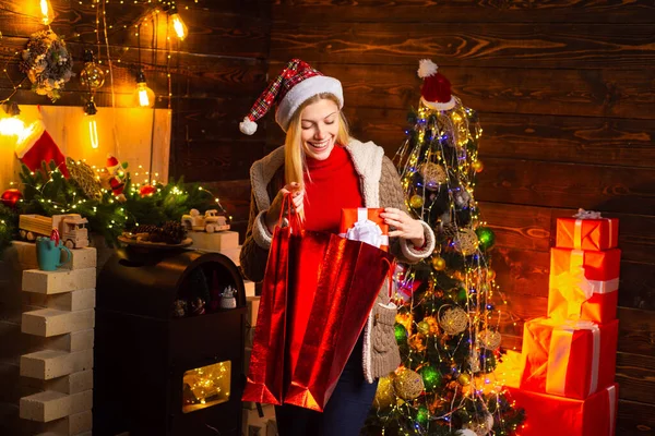 Kadın Noel hediye çantasına bakıyor. Noel elbisesi giymiş güzel bir kadının portresi Noel ağacı arkaplanından yukarı bakıyor. Yeni yıl kavramı.