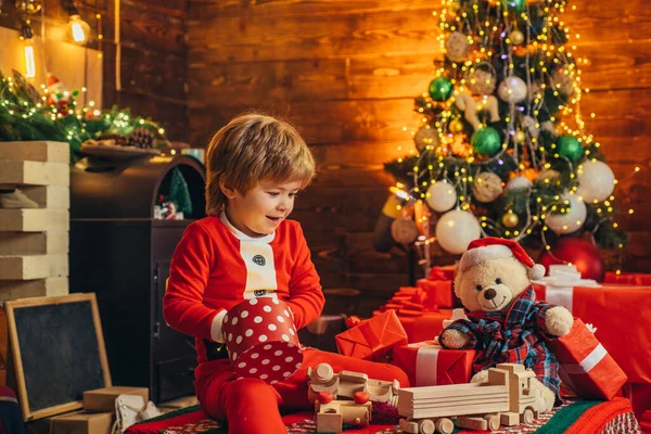 Criança feliz está brincando com caixas de presente de Natal no fundo da árvore de Natal. O miúdo está à espera do Ano Novo. Feriados . — Fotografia de Stock