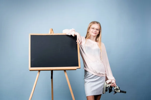 First of September. Day of knowledges. Cute blonde girl standing near blackboard wearing a school uniform. Pretty little schooler girl going to her first lesson. — Stock Photo, Image