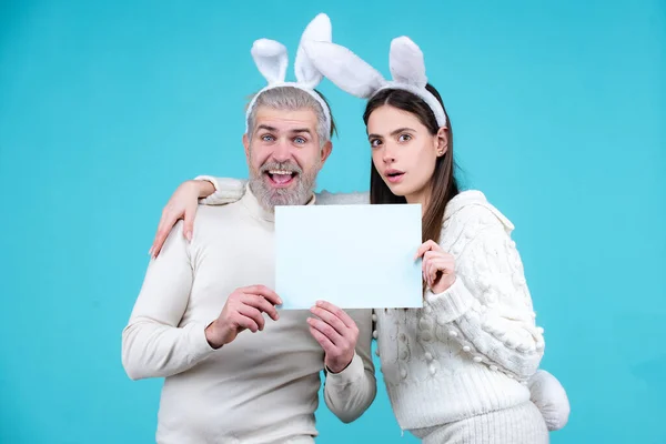 Påskpar som har kul med kaninöron. Påskäggsjakt. Bunny par hålla ombord papper för text. Familjen firar påsk. — Stockfoto