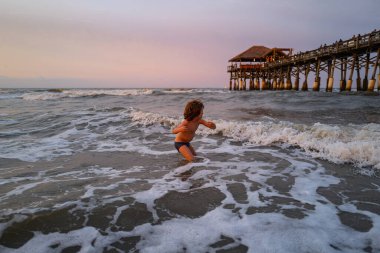 Sahildeki deniz çocuğu. Çocuk mavi denizde dalgalarla oynuyor. Seyahat ve macera konsepti.