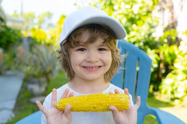 Um rapazinho feliz a comer milho na espiga. Comida para crianças . — Fotografia de Stock