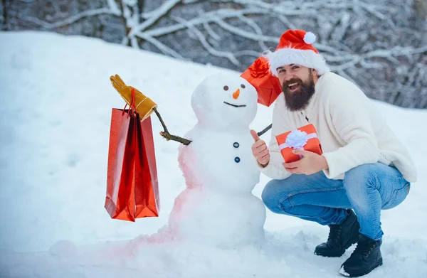 Beau Winter Man avec cadeau et bonhomme de neige dans le parc hivernal givré. Père joyeux tenir cadeau et avoir du plaisir avec bonhomme de neige dans Winter Park. Bonne période hivernale . — Photo