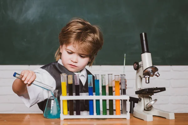 Il ragazzo sta imparando in classe sullo sfondo della lavagna. Giorno della conoscenza. Piccolo scienziato felice che fa esperimento con la provetta — Foto Stock