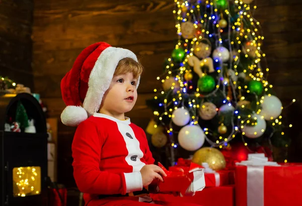 Weihnachtskinder. Weihnachtskind mit roter Geschenkschachtel. Weihnachtskinder - Glückskonzept. Fröhlich süßes Kind öffnet ein Weihnachtsgeschenk. — Stockfoto