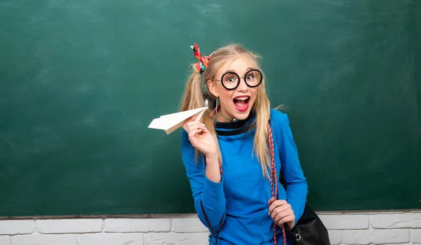 Sınıfta kağıttan uçağı olan genç bir lise öğrencisi. Gözlüklü komik kız. Okuldaki çekici kız kağıt uçakla oynuyor ve gülümsüyor. Üniversite öğrencisi tahtada poz veriyor. — Stok fotoğraf