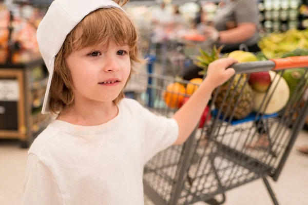 Sale, consumerism and people concept - happy little child with food in shopping cart at grocery store. — Stock Photo, Image