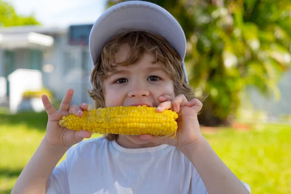 Miúdos a comer milho. Comida para crianças. Bonito menino comer comida saudável no fundo da natureza . — Fotografia de Stock