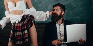 Sakallı yakışıklı koç dizüstü bilgisayarını ve yarı çıplak seksi kız öğrencisini tutuyor. Beyaz sutyen ve ekose etekli baştan çıkarıcı seksi kız öğrenci. Seksoloji ve cinsel davranış dersleri.