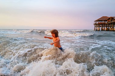 Arka planında beyaz büyük dalgalar olan mavi okyanus. Doğadaki çocuklar güzel deniz, kum ve mavi gökyüzü. Çocuk dışarıda yüzmeyi öğreniyor. Yaz tatili ve seyahat konsepti.