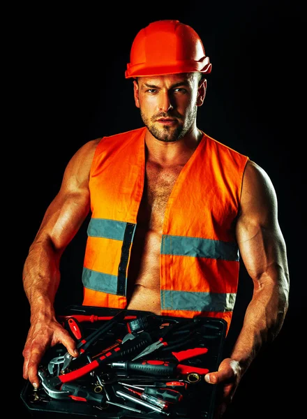 Construtor sexy masculino em chapéu duro. Retrato de homem musculoso em pé sobre fundo preto. Arquitetura e construção industrial . — Fotografia de Stock