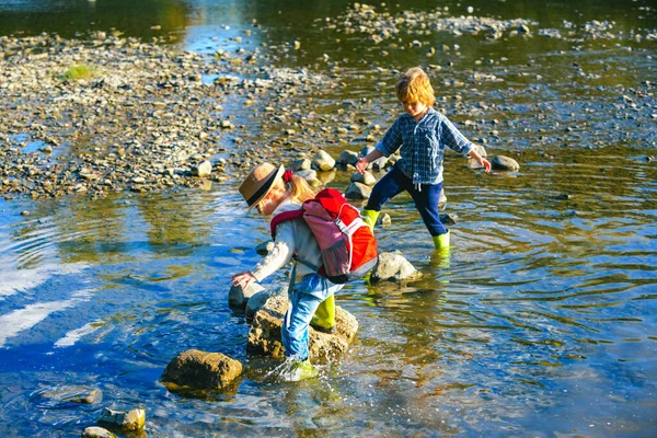Deux enfants avec un sac à dos se tient près d'une rivière de montagne. Garçon et fille regardent le ruisseau. Les enfants traversent la rivière. Voyager avec des enfants . — Photo