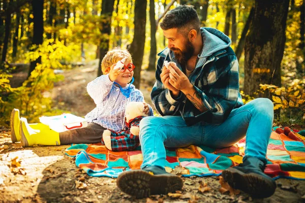 Happy family time outside at fall nature forest. Bearded father play with his toddler son a doctor game. Dad and kid in the park. Beginning of autumn. Family photo concept.