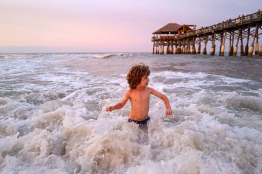 Mutlu çocuk gün batımında denizde oynuyor. Yaz tatilinde tropik sahil adasında açık havada oynayan bir çocuk suya atlıyor..
