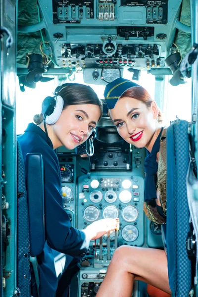 Two beautiful women pilot wearing uniform. Looking at camera through the cockpit. Pilots in cockpit. Girls looking at camera. Happy and successful flight. Couple Women Pilot Sitting in Cabin.