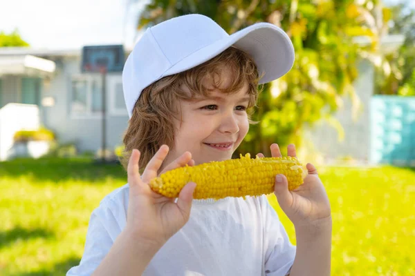 Rapaz a divertir-se com comida legumes milho. Criança no jardim, milho - menino adorável comendo milho na espiga no jardim . — Fotografia de Stock